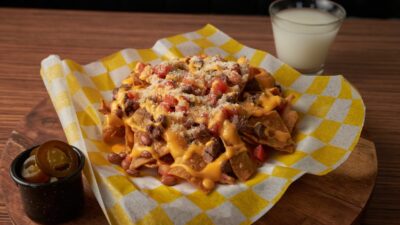 Delicious cheesy nachos topped with jalapeños served on a wooden platter with a drink.